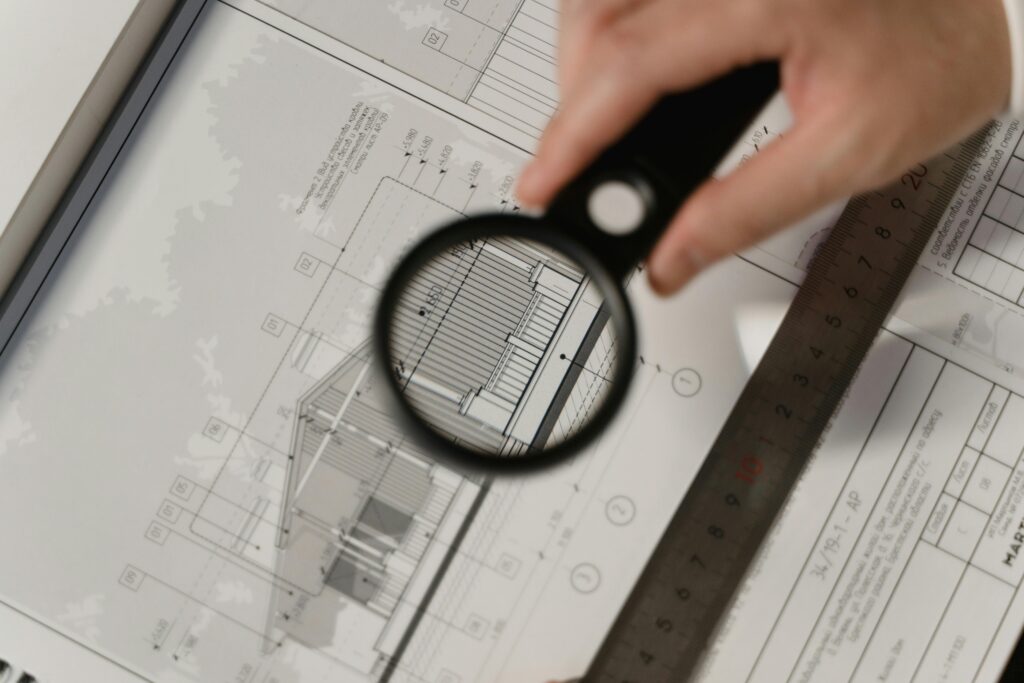 Magnifying glass inspecting architectural plans with a ruler, related to building inspection business.